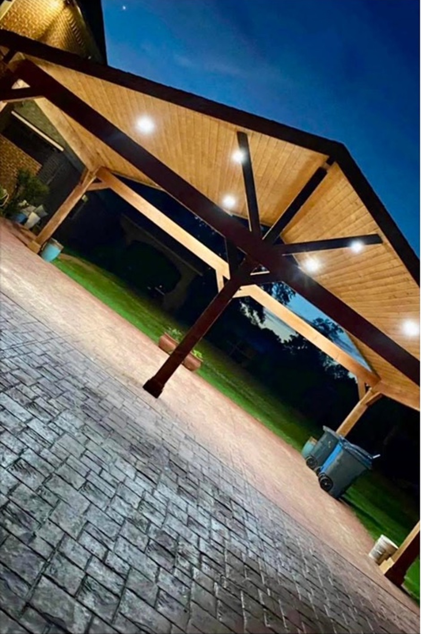 Stamped concrete patio beneath a custom cedar covered pavilion lit at dusk